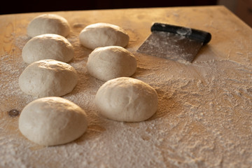 Fototapeta na wymiar Stay at home for coronavirus covid-19 lockdown concept: make pizza at home. Backlit low angle view of leavened dough portions ready to bake on a light wooden work table dusted with flour