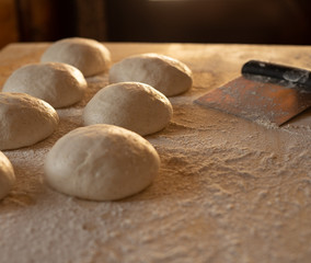 Stay at home for coronavirus covid-19 lockdown concept: make pizza at home. Backlit low angle view of leavened dough portions ready to bake on a light wooden work table dusted with flour