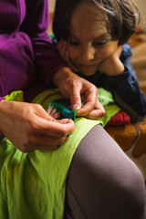 A woman sews a patch on torn clothes from an old sock.