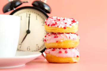 Donuts in pink grazury, next to a cup of coffee, espresso and a black alarm clock. Snack time, not time for sweets. Place for text. Vertical orientation