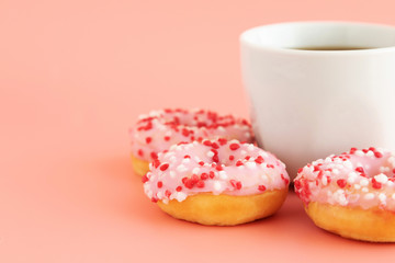Three donuts in pink glaze with decoration lie around a cup of coffee or espresso. Coffee concept. Place for text. Brunch, lunch, sweet snack