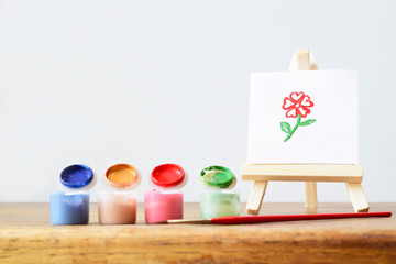 Drawing or painting flower on white sheet paper on easel for painter on the table with water color and brush. Creative idea and education concept.