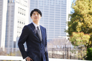 Fototapeta na wymiar ビルを背景に立つ日本人男性ビジネスマン
