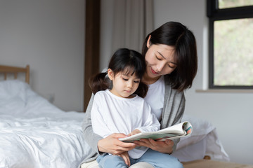 Young Asian mother is reading a book with her daughter