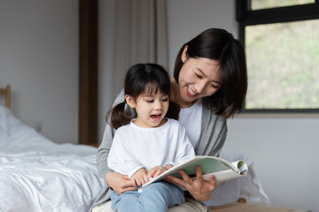 Young Asian mother is reading a book with her daughter - obrazy, fototapety, plakaty