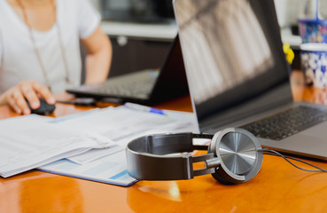 Headphones and laptop computer table with blurred woman working in background work from home concept.
