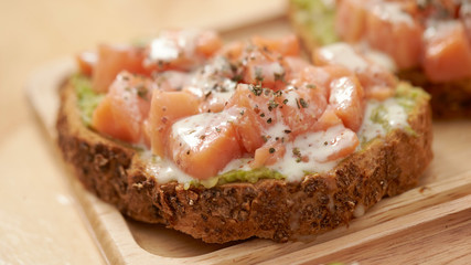 Salmon, avocado paste and white sauce on slice of baguette