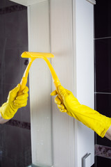 
Cleaning the bathroom mirrors. A hand in a yellow glove washes a mirror with glass scraper.