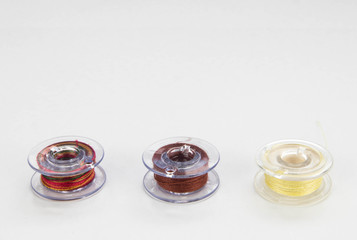 Close up of a groups of three sewing machine bobbins with colourful thread on a white background.