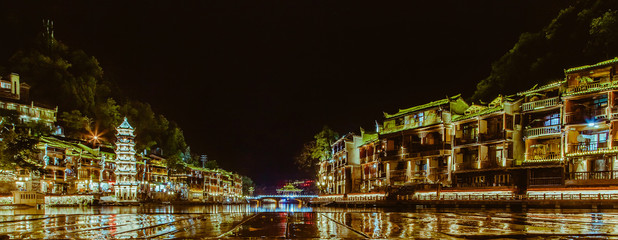 View of illuminated at night riverside houses in ancient town of Fenghuang known as Phoenix, China. Selective focus.