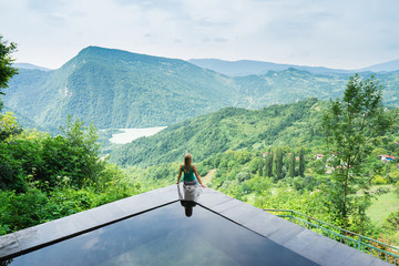 Woman sitting on the edge of swiming pool  on the top of mountain. Lailashi, Racha, Georgia.