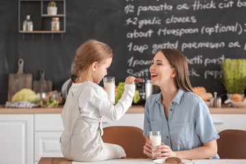 Mother with her little daughter drinking milk with cookies in kitchen