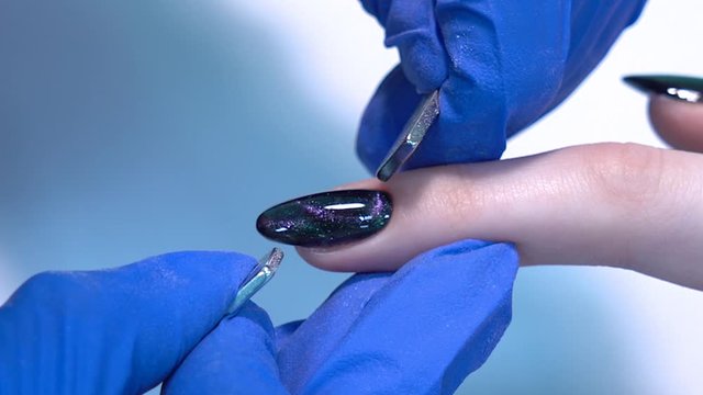 Closeup view 4k video of professional colorful glossy brilliant holiday manicure at fingers of young woman. Modern trendy shiny amazing cat eye effect nail design on black gelpolish.