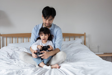 Young Asian dad is playing games on bed with daughter