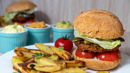 Vegan burger closeup with sliced tomatoes, pickled cucumbers, lettuce and baked potatoes. Homemade comfort plant based food. Cooking at home.