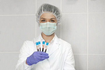 Fototapeta na wymiar Young sexy female doctor in protective mask and rubber gloves holds four blood test tubes in scientific medical laboratory. Lab diagnostics biochemical analysis concept. Focus on blood samples