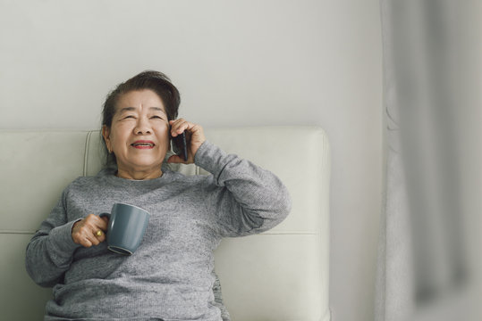 Happy Asian senior woman talking a phone and holding drink cup, stay home stay safe concept.