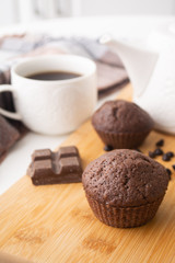 Chocolate muffins, chocolate chips, chocolate bar, a cup of coffee, teapot on a wooden surface with a warm scarf, Christmas lights bokeh and holly in the background