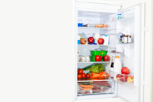 Top freezer kitchen refrigerator with doors open and shelves full of groceries with fresh and frozen food and cold bottles