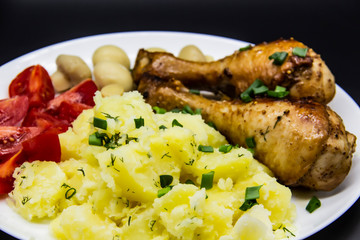 Tasty cooked chicken legs with potatoes, tomatoes, mushrooms on a white plate. Delicious potatoes with onion and dill on dinner, lunch. Amazing chicken legs cooked in spice. Ukrainian healthy meal