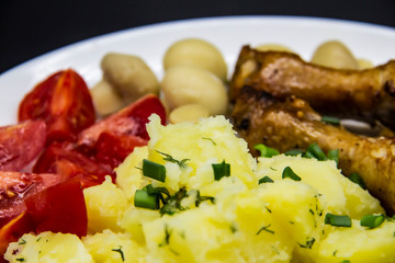 Tasty cooked chicken legs with potatoes, tomatoes, mushrooms on a white plate. Delicious potatoes with onion and dill on dinner, lunch. Amazing chicken legs cooked in spice. Ukrainian healthy meal