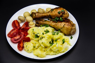 Tasty cooked chicken legs with potatoes, tomatoes, mushrooms on a white plate. Delicious potatoes with onion and dill on dinner, lunch. Amazing chicken legs cooked in spice. Ukrainian healthy meal