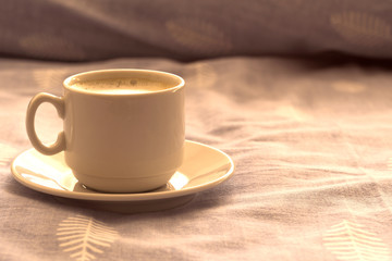 a cup of morning coffee in bed. a cup of coffee on a saucer stands on the bed in the morning sun. morning awakening.