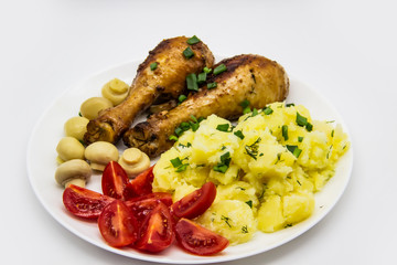 Tasty cooked chicken legs with potatoes, tomatoes, mushrooms on a white plate. Delicious potatoes with onion and dill on dinner, lunch. Amazing chicken legs cooked in spice. Ukrainian healthy meal