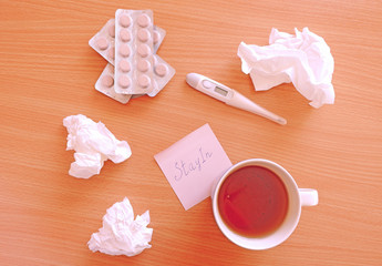 Flat lay with cup of tea, paper napkins, electronic thermometer, pills and stay in note on wooden table