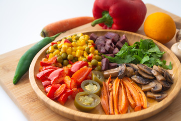 Nutritious and healthy buddha fajita bowl with sweet corn, green peas, red bell pepper, jalapenos, carrots, mushrooms, spinach, beetroot and sweet potatoes surrounded by ingredients and lemon
