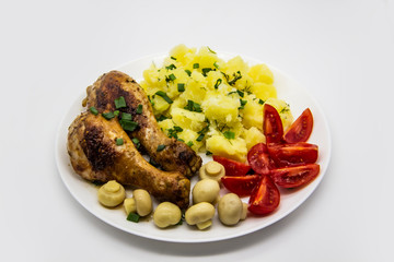 Tasty cooked chicken legs with potatoes, tomatoes, mushrooms on a white plate. Delicious potatoes with onion and dill on dinner, lunch. Amazing chicken legs cooked in spice. Ukrainian healthy meal