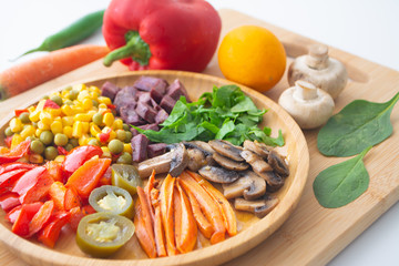 Nutritious and healthy buddha fajita bowl with sweet corn, green peas, red bell pepper, jalapenos, carrots, mushrooms, spinach, beetroot and sweet potatoes surrounded by ingredients and lemon
