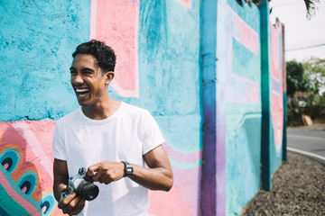 Laughing Hispanic man in casual clothes with camera on street