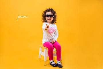 Fototapeta na wymiar Little girl shows two fingers, gesture of peace on a yellow background