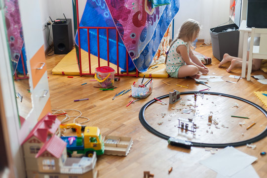 A real mess in the kids room. A girl plays among scattered toys.