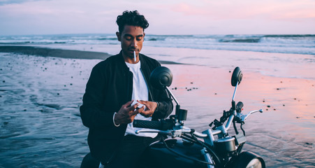 Young man on motorbike smoking on seashore