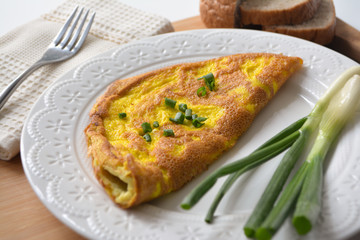 Fluffy breakfast omelette with green spring onions and fresh toast bread on a wooden surface with a napkin and metal fork