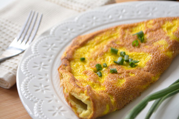 Fluffy breakfast omelette with green spring onions and fresh toast bread on a wooden surface with a napkin and metal fork