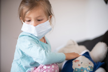 Young girl in mask playing doctor with teddy 