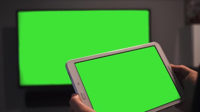 Women Hands Using Tablet in Front of the With Isolated Green Croma Key Screen. Green Screen Tablet Close Up and Watching Television Green Screen. Whach Tv  in the Two Screens Concept
