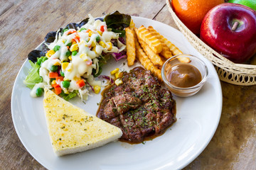 Grilled steaks in white dish on old wooden table, baked potatoes and vegetable salad