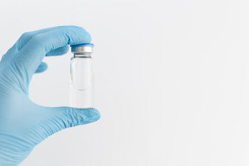 Doctors hand in blue rubber glove holding medicine bottle with blue cover and clear fluid on grey...