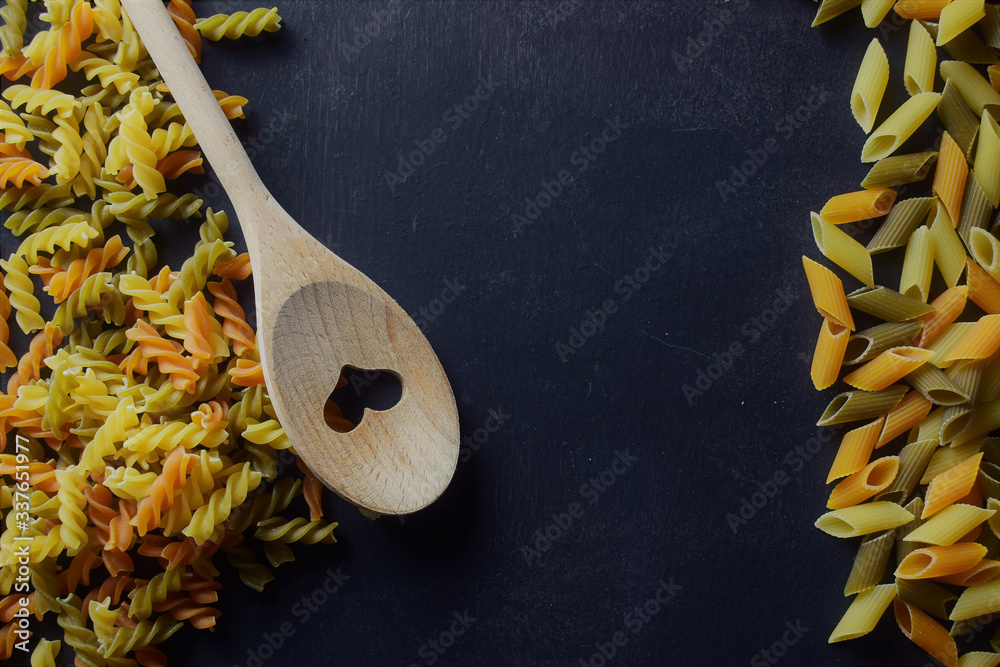 Wall mural wooden spoon on slate, with two varieties of colored pasta on both sides, spirals and macaroni