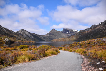 Fototapeta na wymiar The road near dry grass field with snow mountain and cloudy blue sky background on sunny day in Tasmania, Australia