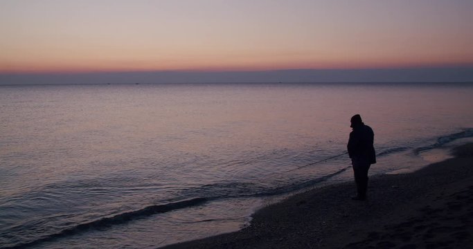 Long shot angler facing ocean, protective winter gear, sunrise, Almeria, Spain