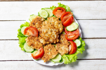 Chicken fritters garnished with salad leaves, tomato, cucumber on white wooden background