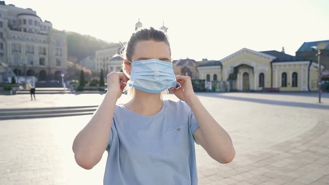 Woman standing at the almost emty city square and wearing face mask. Slowmotion. Stedicam shot.