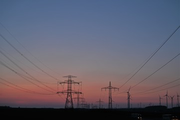 Fototapeta na wymiar Strommasten einer Stromstrasse mit perspektivisch verlaufenden Stromkabeln bei Abenddämmerung mit rotem Himmel