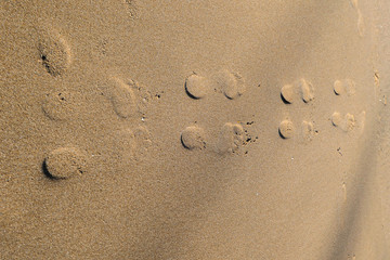 Fototapeta na wymiar Yellow sand on the beach with shapes of feets.