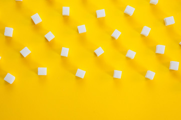 Fototapeta na wymiar Refined sugar cubes shot on a yellow background. Background for sweets, food and drinks.